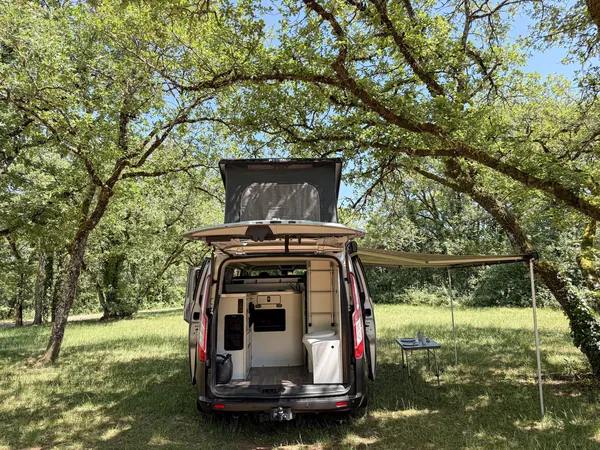 Store déployé à l'arrière du van avec table et chaises pour la vie extérieure